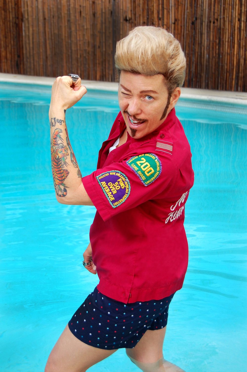 Drag King Mo B. Dick mit den Beinen im Pool, zeigt einen gebeugten starken Arm und zwinkert in die Kamera | © Dave Morphy